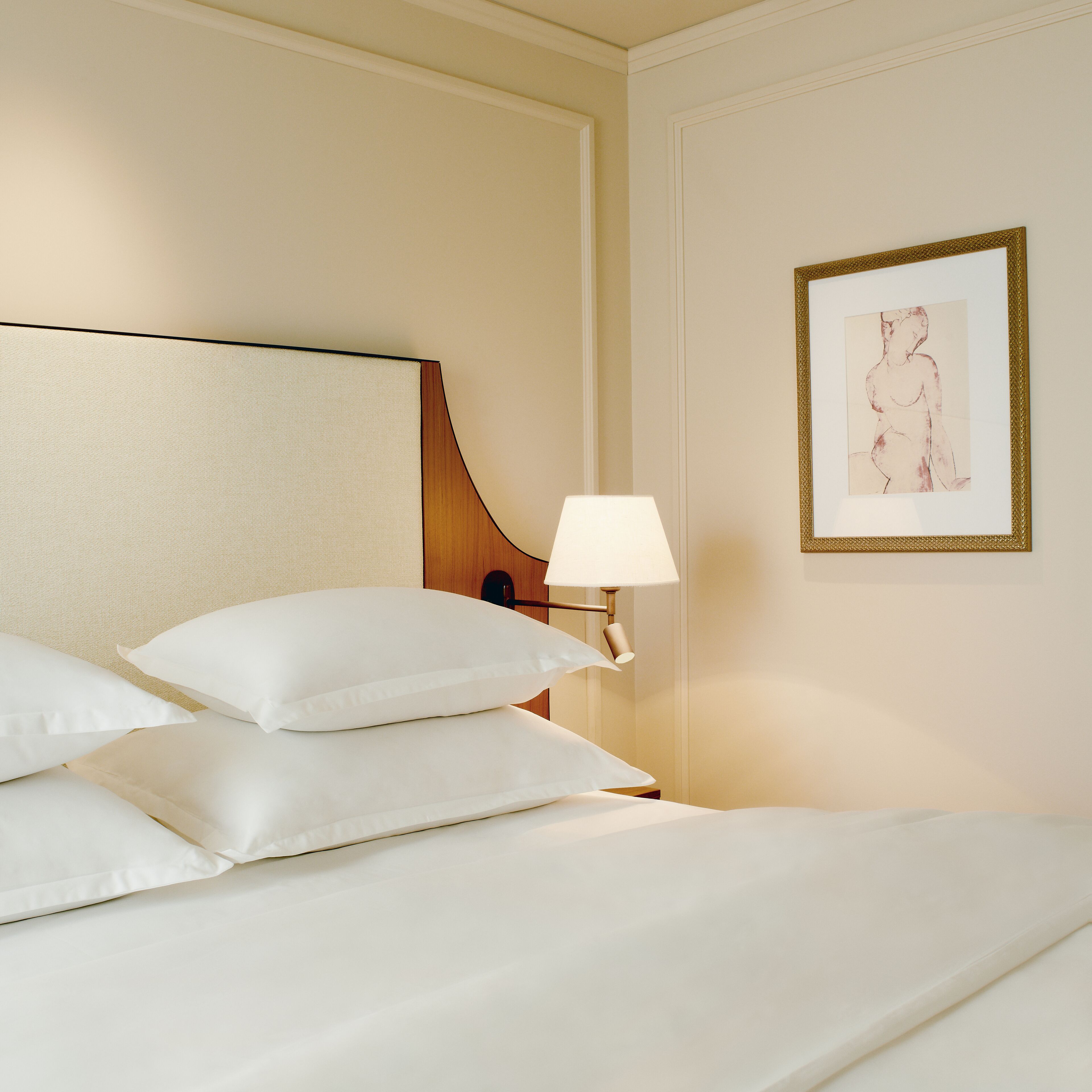 A neatly made bed with white linens and pillows, a bedside lamp, and a framed artwork on the wall.