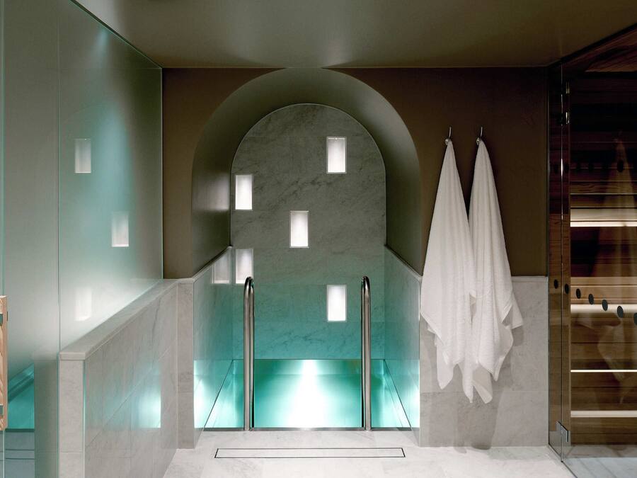 Un baño moderno con ducha de vidrio, paredes de mármol y un banco de madera.