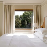 A hotel room with a large bed, a window with curtains, and a view of trees outside.