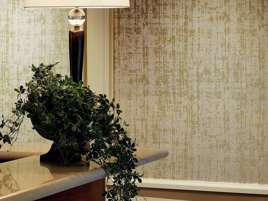Una lámpara con pantalla blanca sobre una superficie de madera, una planta en maceta y una pared con textura.