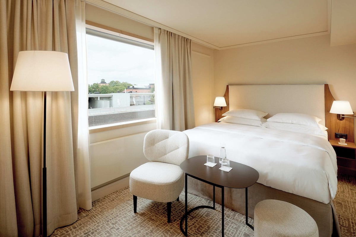 A hotel room with a large bed, two bedside tables with lamps, a small round table, and a chair.