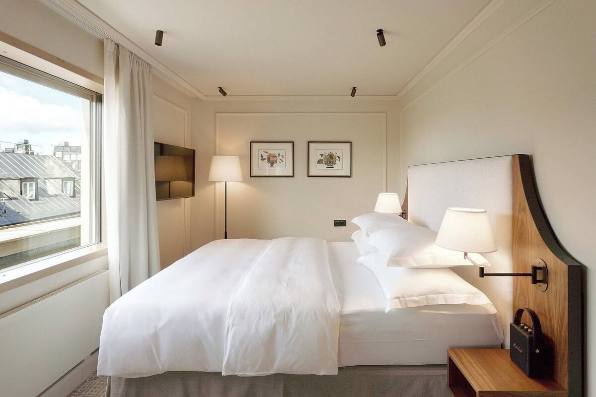 A hotel room with a large bed, two bedside lamps, a wooden nightstand, and two framed pictures on the wall.