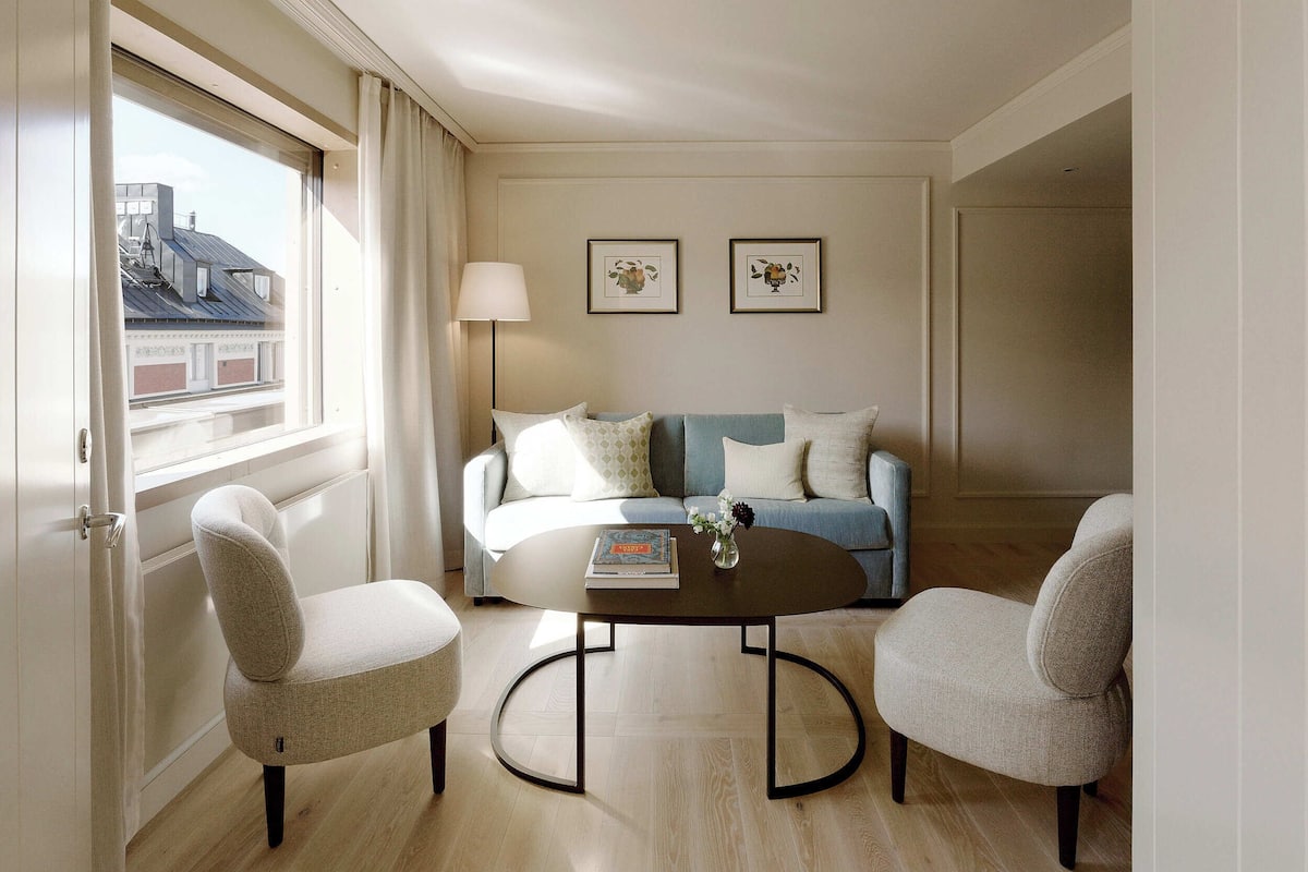 A modern living room with a sofa, two armchairs, a coffee table, and a window with curtains.