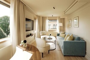 Un salón moderno con un sofá azul, una mesa de centro redonda y un sillón color beige. Una ventana con cortinas deja entrar luz natural.