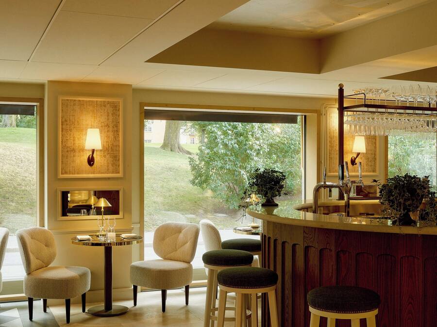 A bar area with a wooden counter, bar stools, and a large window offering a view of greenery outside.