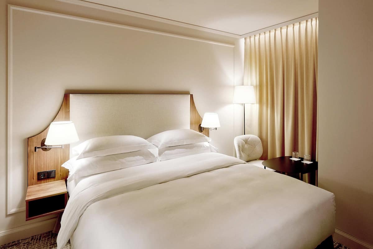 A hotel room with a large bed, two bedside tables with lamps, a chair, and a window with curtains.