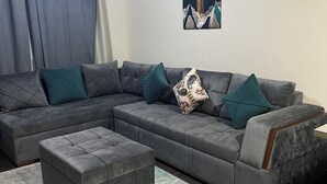 A modern living room with a grey sectional sofa, teal cushions, and a patterned throw pillow. A grey ottoman is in front of the sofa, and a painting hangs on the wall. - Porto sharm elsheikh  (Sharm El Sheikh)