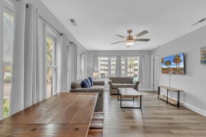 A spacious living area with a large wooden table, two sofas, a ceiling fan, and large windows with curtains. - Island palms (North Myrtle Beach)