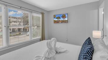 A hotel room with a large bed, a painting of palm trees, and a view through the window.