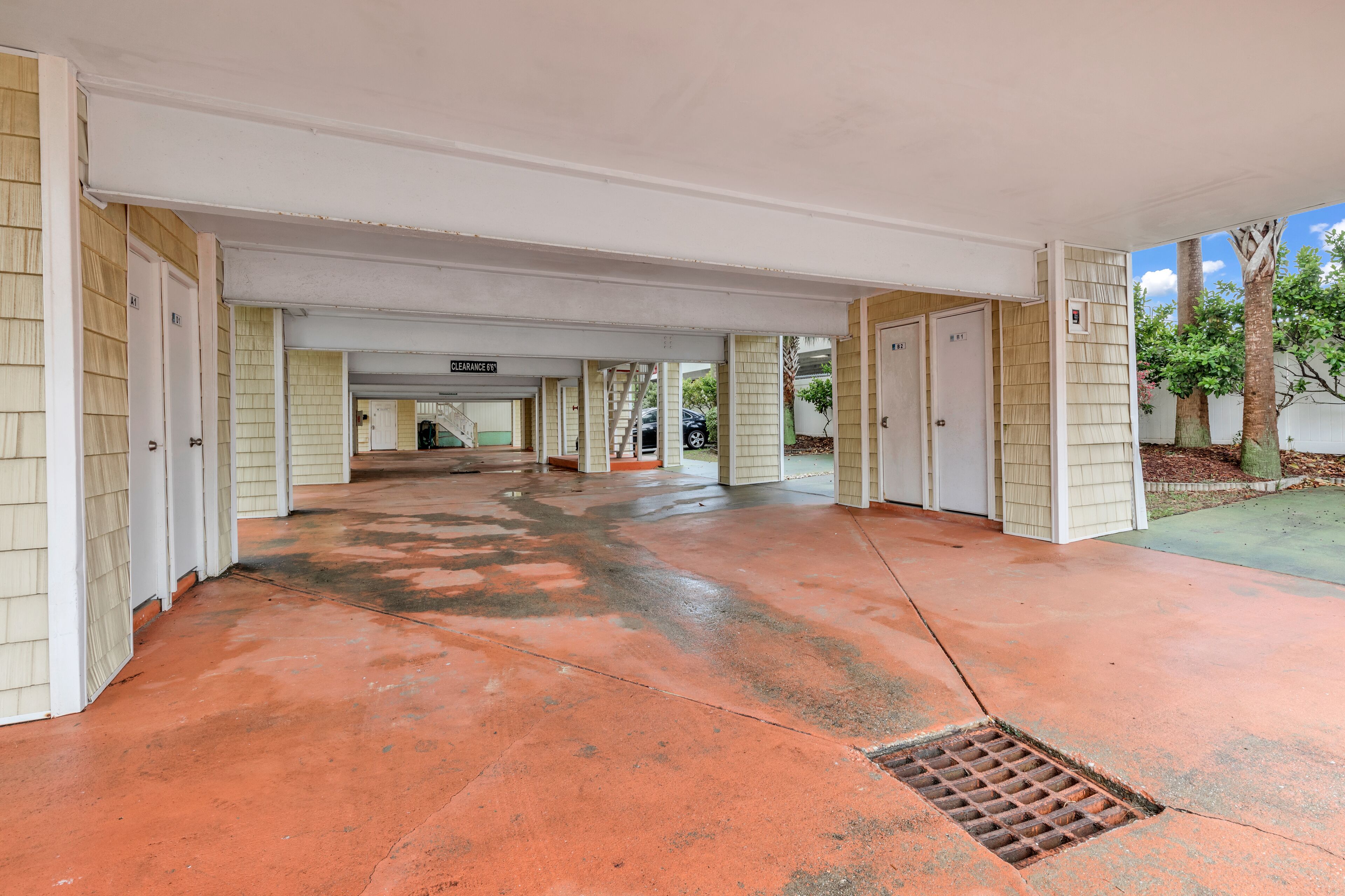 A covered parking area with a red concrete floor and multiple doors leading to individual units.