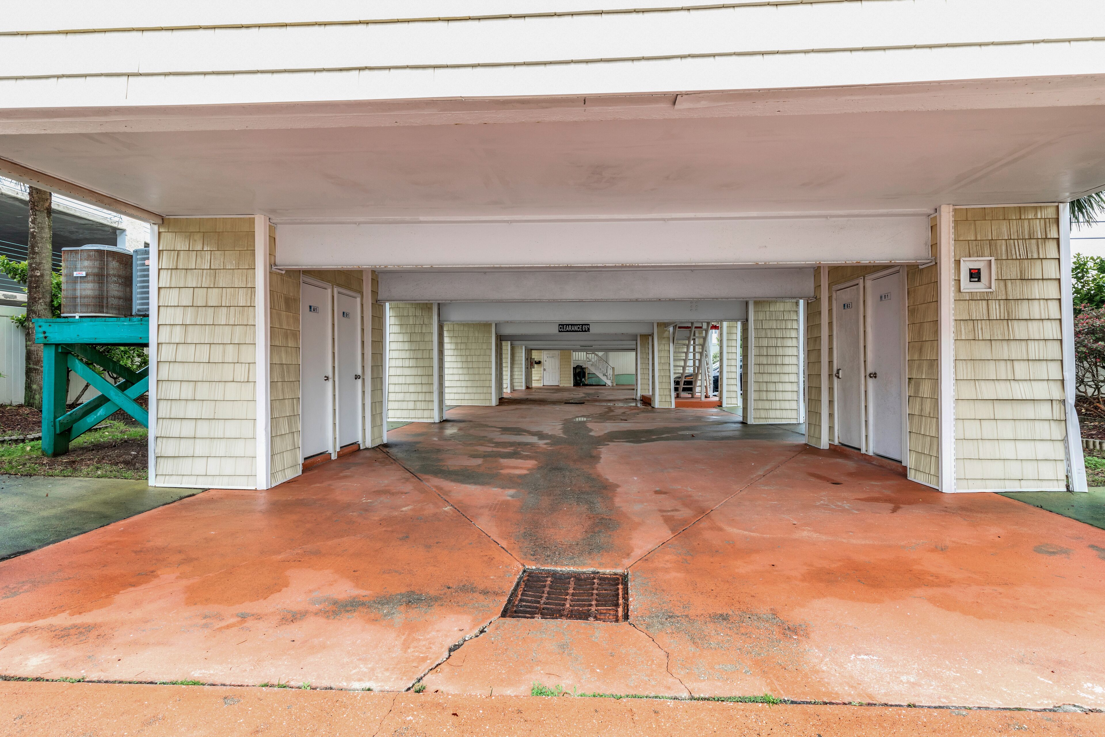A covered walkway leading to a building with multiple doors, a metal vent, and a green structure to the left.