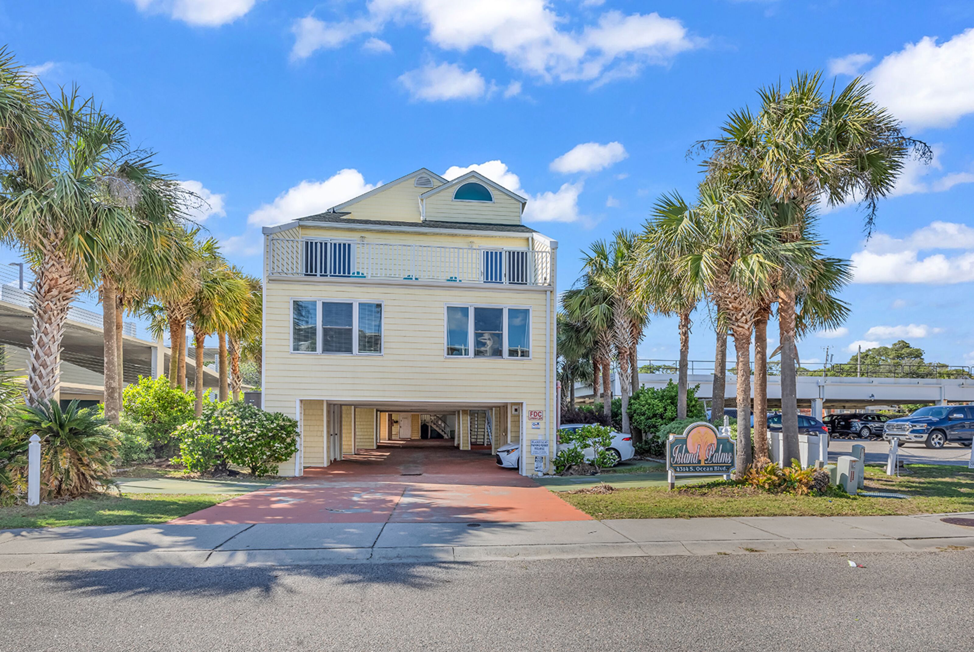 A two-story building with a red entrance walkway, surrounded by palm trees and a clear blue sky.