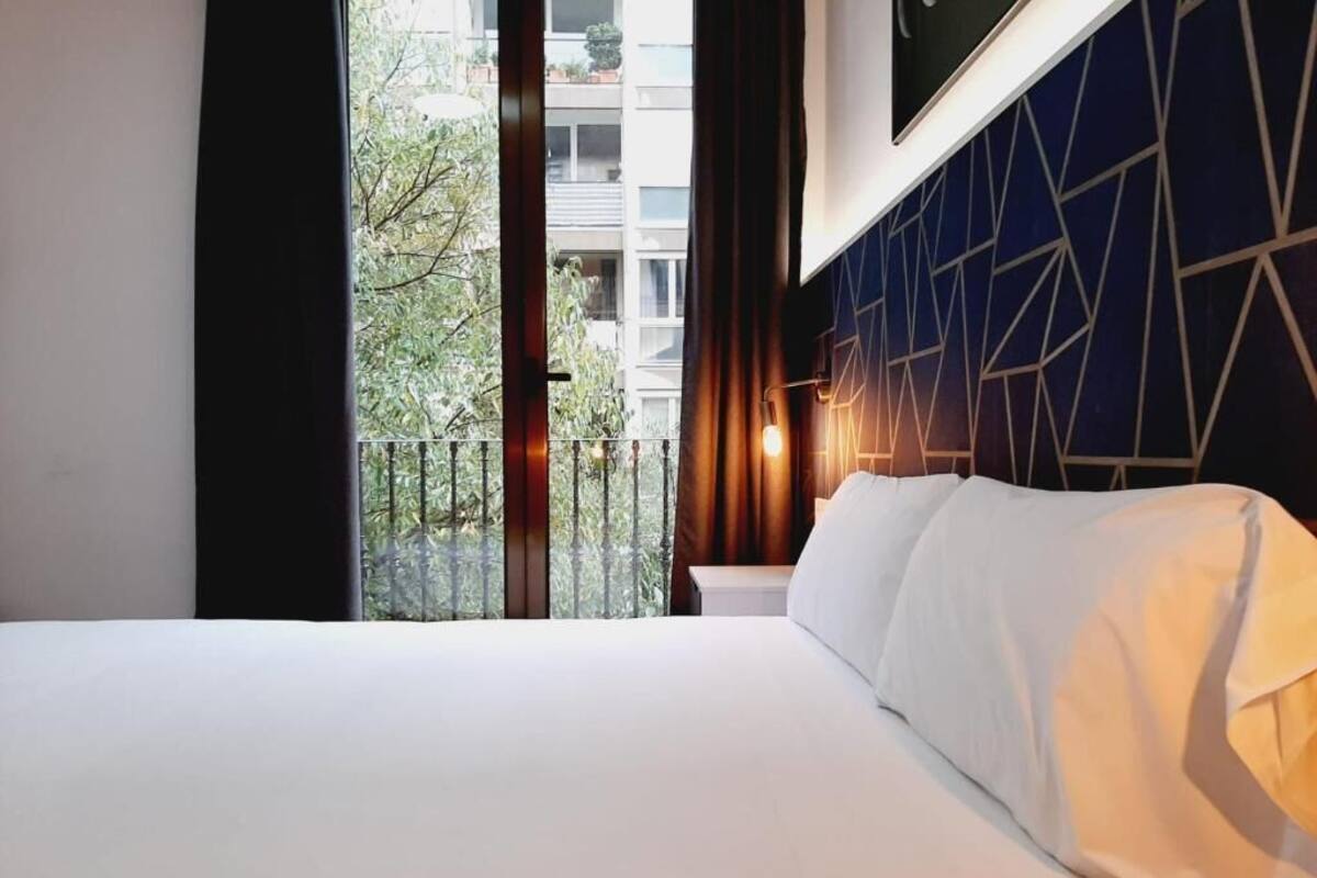 Ein Hotelzimmer mit Bett, Balkonblick und Wand mit geometrischem Muster.