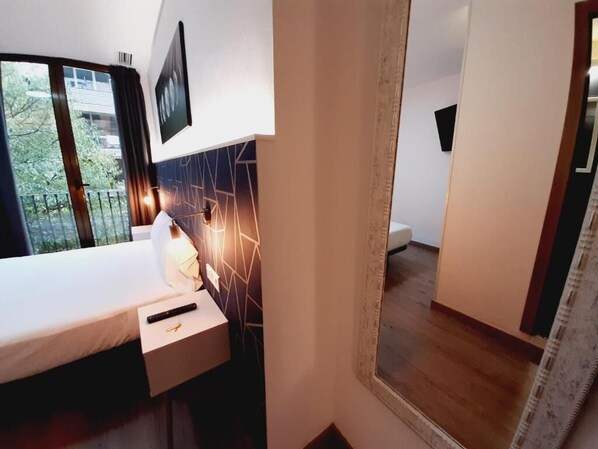 Une chambre d’hôtel avec un lit, une table de chevet, un miroir et une vue sur l’extérieur.