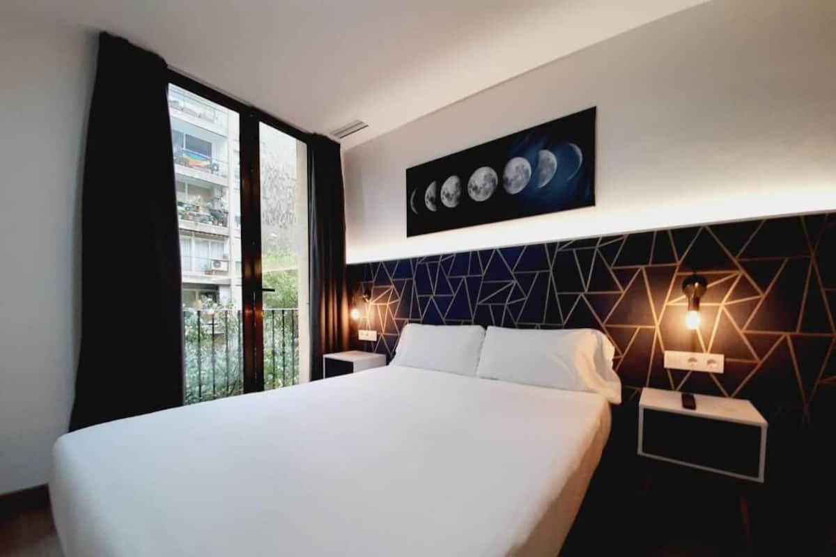 Ein modernes Hotelzimmer mit einem großen Bett, einem Kopfteil mit geometrischem Muster und einem Wandbild, das die Mondphasen zeigt.