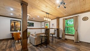 Una habitación acogedora con techo de madera, comedor con mesa y sillas, un sofá y una ventana con cortinas.