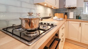 A modern kitchen with a gas stove, stainless steel pot, wooden countertop, and light-colored cabinets. - 11 The Craighurst (Reydon)