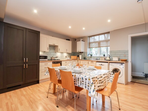 Una cocina moderna con armarios de madera, una mesa de comedor para seis comensales y una lavadora integrada.
