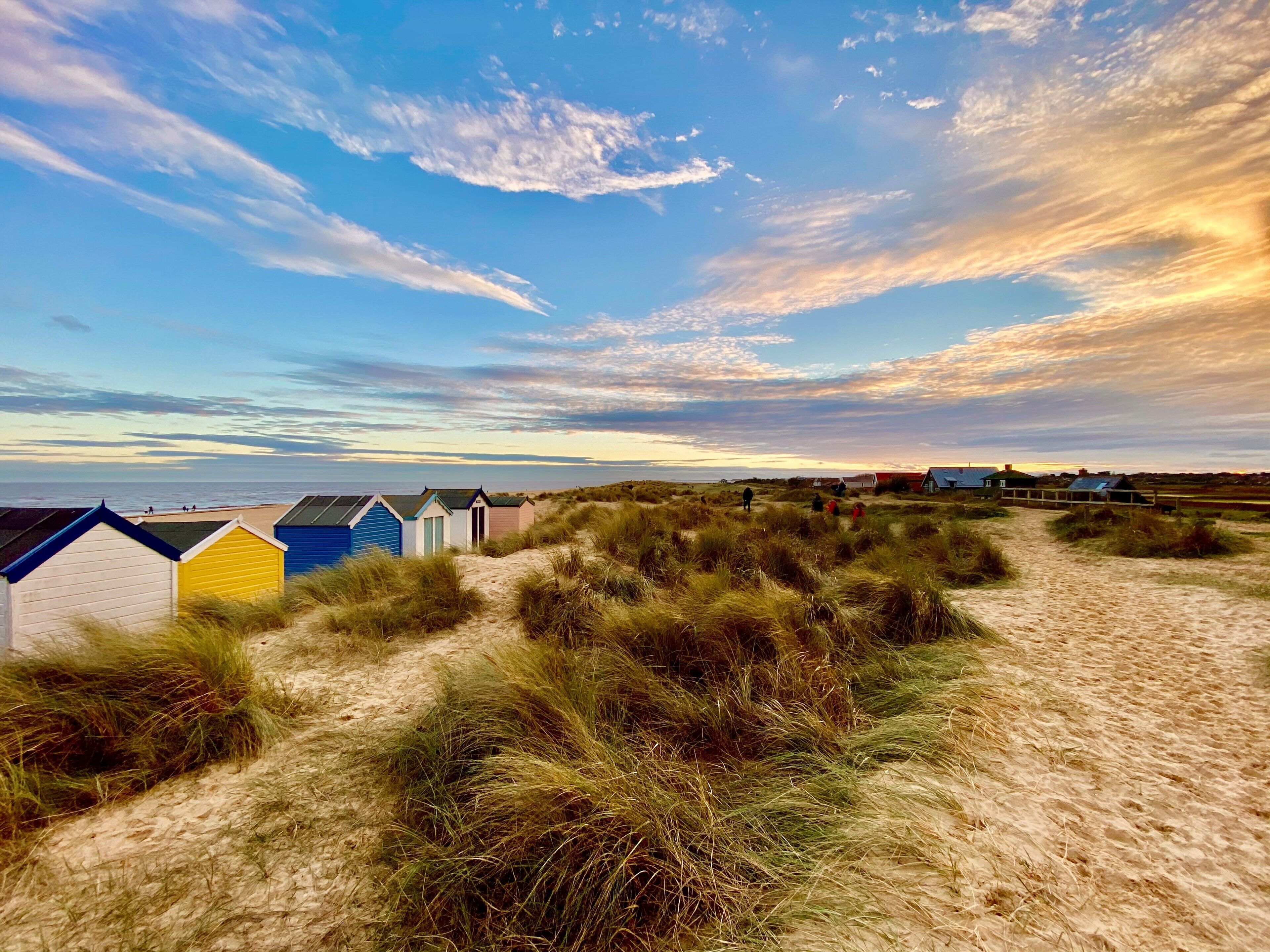 A beach with several beach huts and a path leading through the dunes.