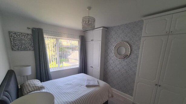 Une chambre à coucher avec un lit, une lampe de chevet, une armoire et une fenêtre avec des rideaux.