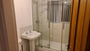 Une salle de bain avec une douche à parois de verre, un lavabo sur colonne et des toilettes.