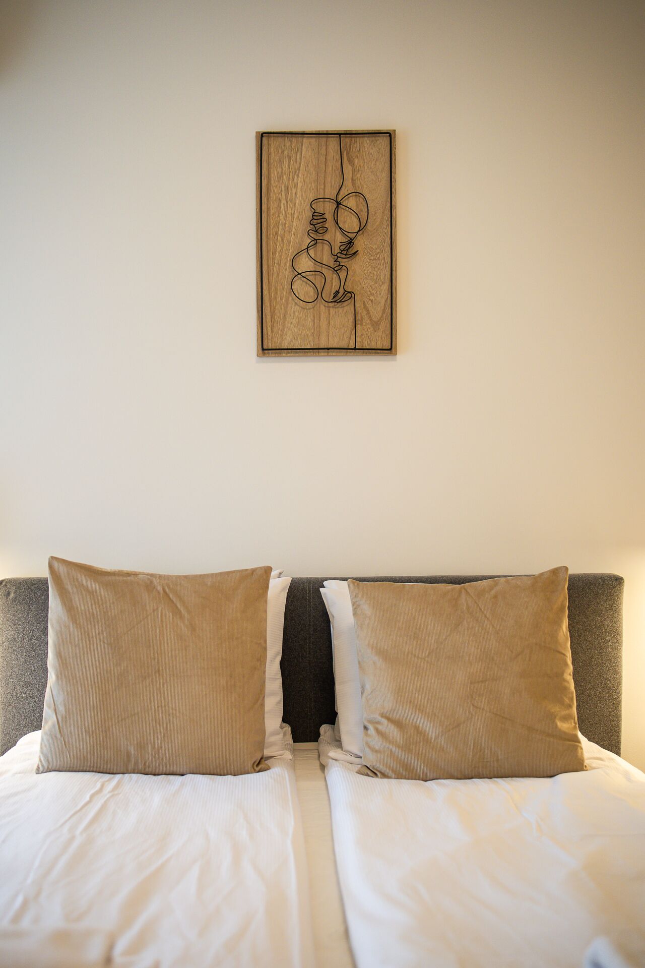 A neatly made bed with two beige pillows and a dark headboard.
