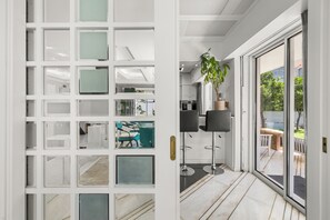 A modern interior with a glass partition, a dining area with bar stools, and a view of the outdoors. - Luxury Villa with Pool,BBQ and Garden Vouliagmeni
 (Voula)