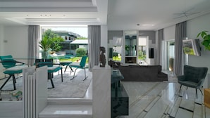 A modern living room with a glass dining area, a sofa, and a TV mounted on the wall. - Luxury Villa with Pool,BBQ and Garden Vouliagmeni
 (Voula)