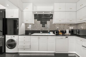 Ett modernt kök med vita skåp, en inbyggd tvättmaskin och ett stänkskydd av granit ovanför bänkskivan.