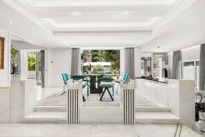 A modern dining area with a glass table and chairs, a view of the outdoors, and a clean, white interior. - Luxury Villa with Pool,BBQ and Garden Vouliagmeni
 (Voula)