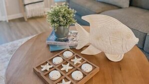 Un tavolino in legno con un gioco a forma di stella marina, una pianta in vaso e una scultura di pesce.