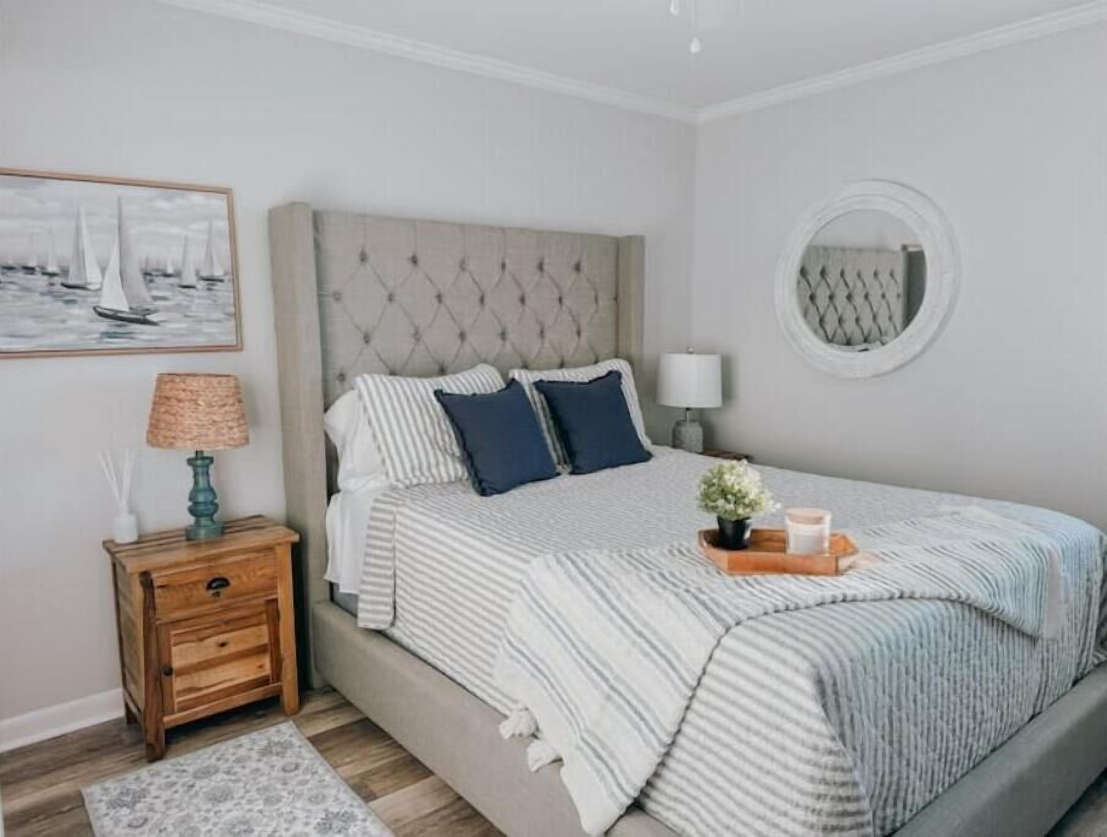 Une chambre à coucher avec un lit, une table de chevet, une lampe, un miroir et un tableau encadré au mur.