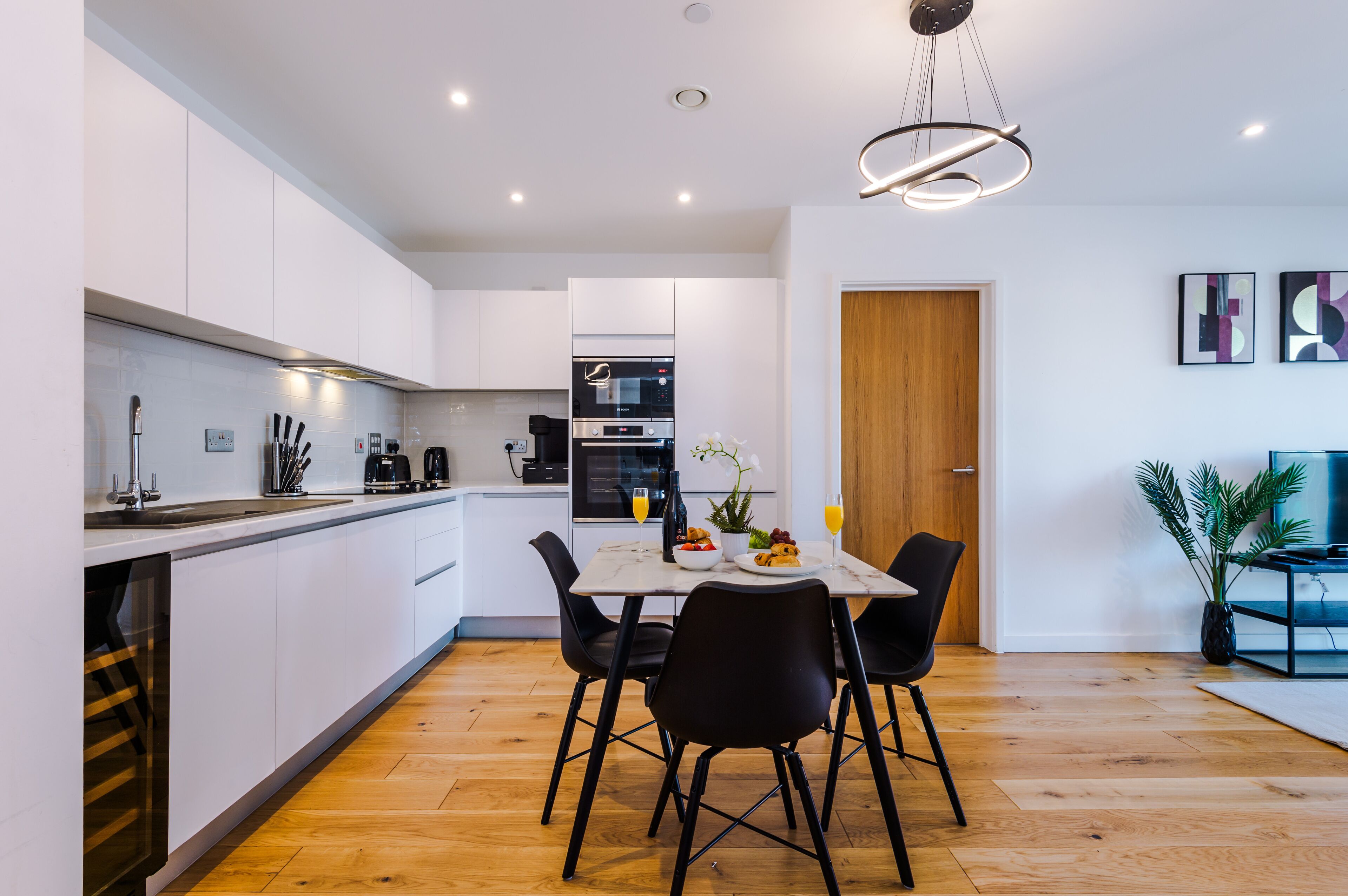 Una cucina moderna con mobili bianchi, un tavolo da pranzo con sedie nere e un pavimento in legno.