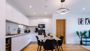A modern kitchen with white cabinets, a dining table with black chairs, and a wooden floor.