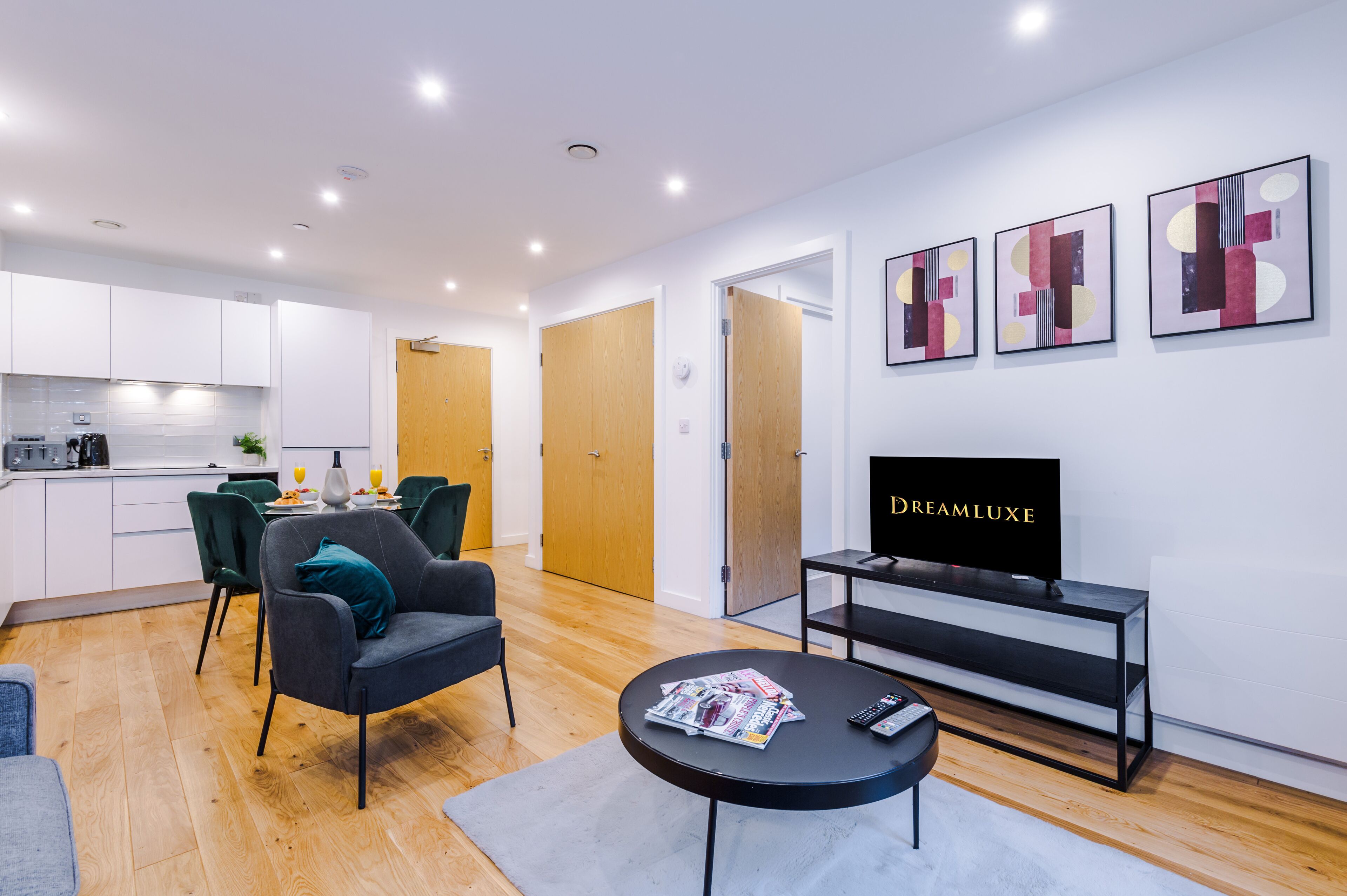 Een moderne woonkamer met een zwart tv-meubel, een eethoek met tafel en stoelen, en een keuken op de achtergrond.