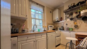 A kitchen with white cabinets, a window, a sink, a stove, and a bar stool. - Beautiful 1-bed Apartment in London (London)