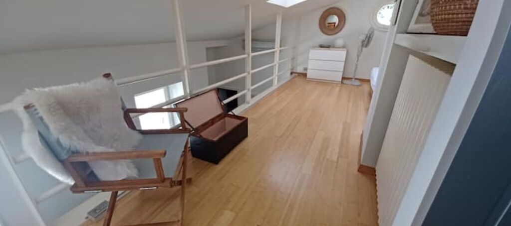 A loft-style room with a high ceiling, a wooden floor, a white chair, a small table, and a white dresser.
