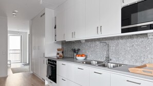 A modern kitchen with white cabinets, a stainless steel sink, and a microwave. - Stylish Urban Home in Stockholm (Stockholms län)
