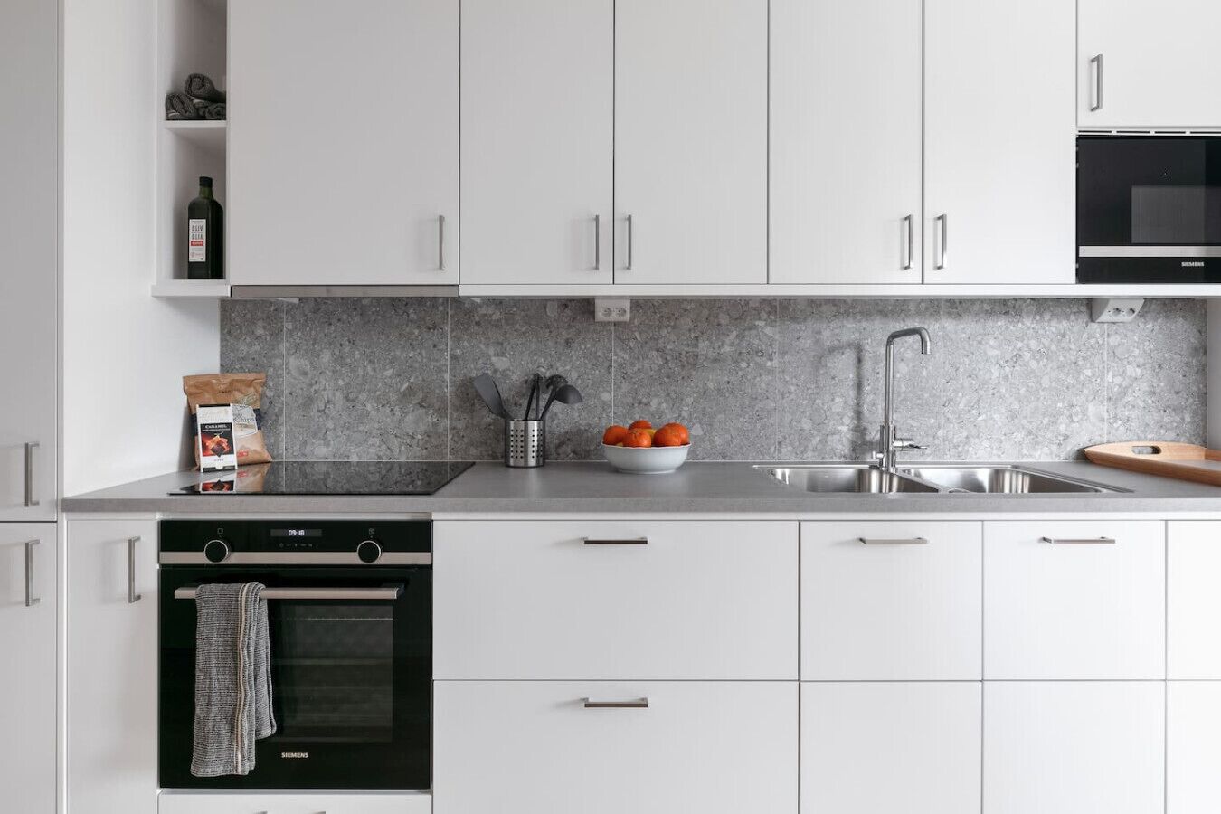 Eine moderne Küche mit weißen Schränken, einer Edelstahlspüle, einer Mikrowelle und einem eingebauten Backofen.