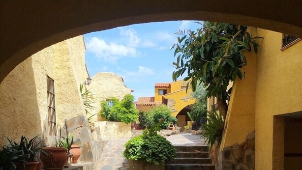 An arched passageway with stone flooring, potted plants, and a view of buildings in the distance. - Casa Lares (Casas de Don Pedro)