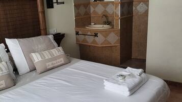 A hotel room with a large bed, a bathroom with a sink and mirror, and a wooden headboard.