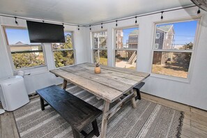 A room with a wooden table and benches, large windows, and a television. - Ocean View, Semi-Oceanfront, Screened In Porch, Beach Access (Avon)