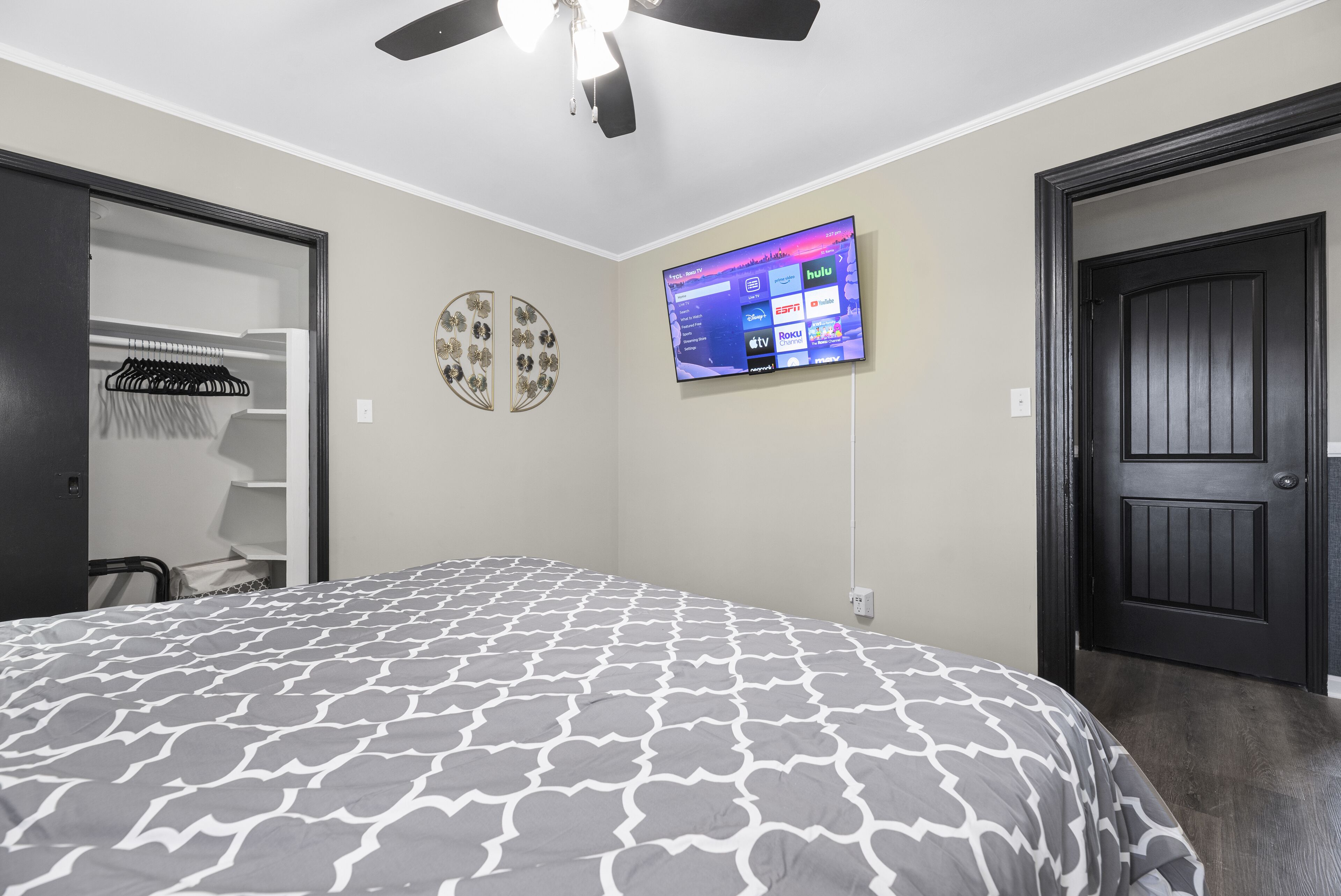 A bedroom with a bed, a TV mounted on the wall, a closet, and a door.