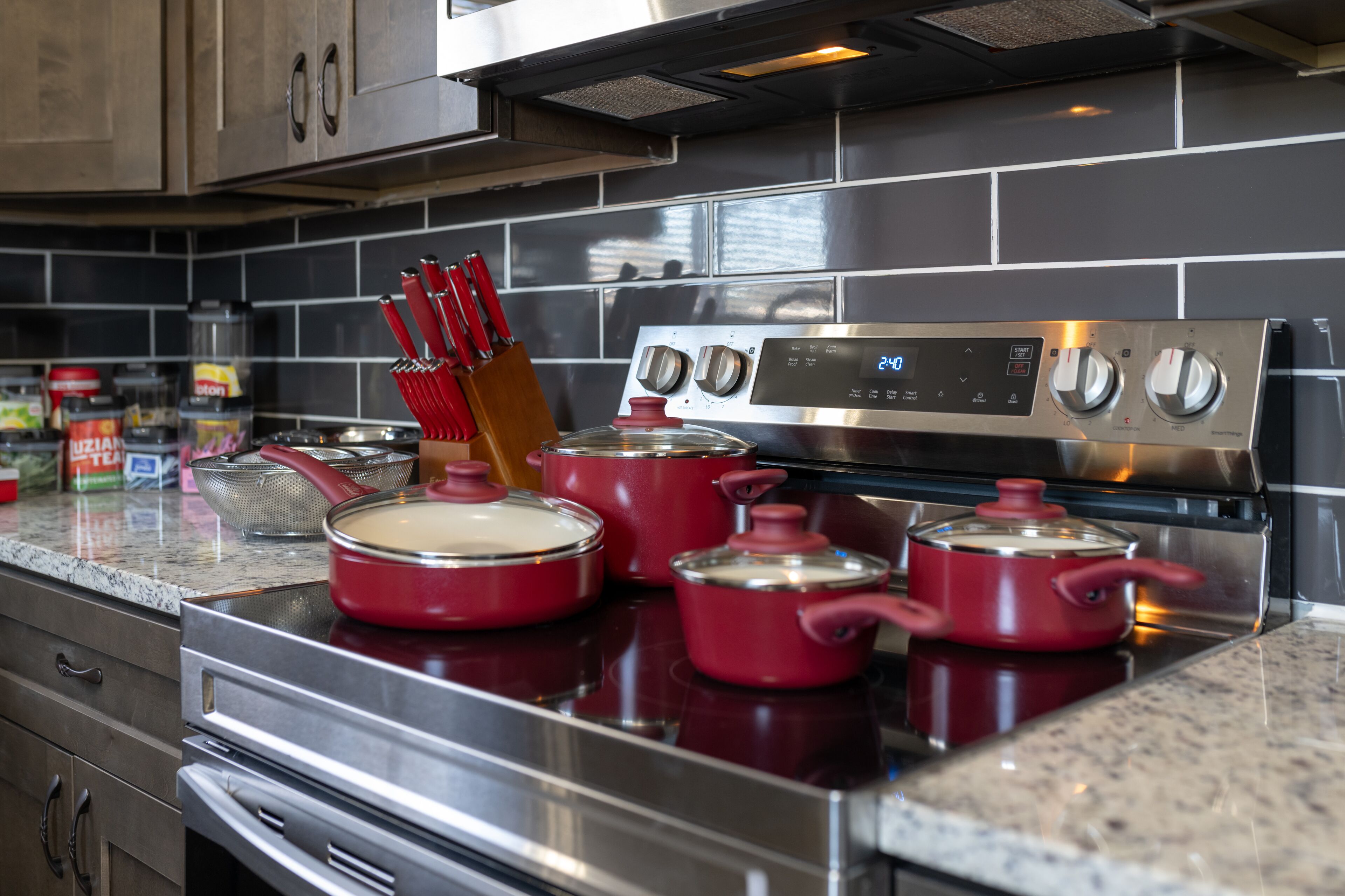 Una cucina con elettrodomestici in acciaio inossidabile, pentole rosse e un rivestimento moderno.