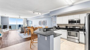 A modern kitchen with stainless steel appliances, a dining area with wicker chairs, and a view to the outside. - *Aug 29 - Sept 3rd Open!* Spacious Condo! (Panama City Beach)