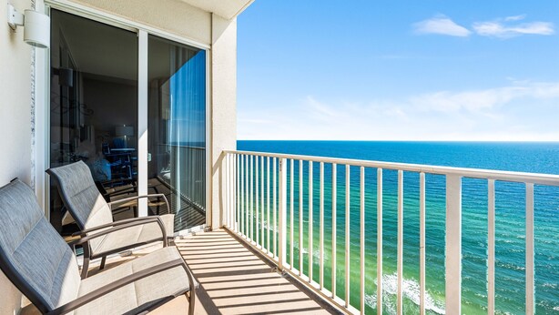 A balcony with two chairs and a table, overlooking a clear blue ocean. - *Aug 29 - Sept 3rd Open!* Spacious Condo! (Panama City Beach)