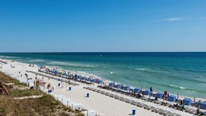 A beach with rows of striped beach umbrellas and lounge chairs, a pier in the background, and a clear blue sky. - *Aug 29 - Sept 3rd Open!* Spacious Condo! (Panama City Beach)