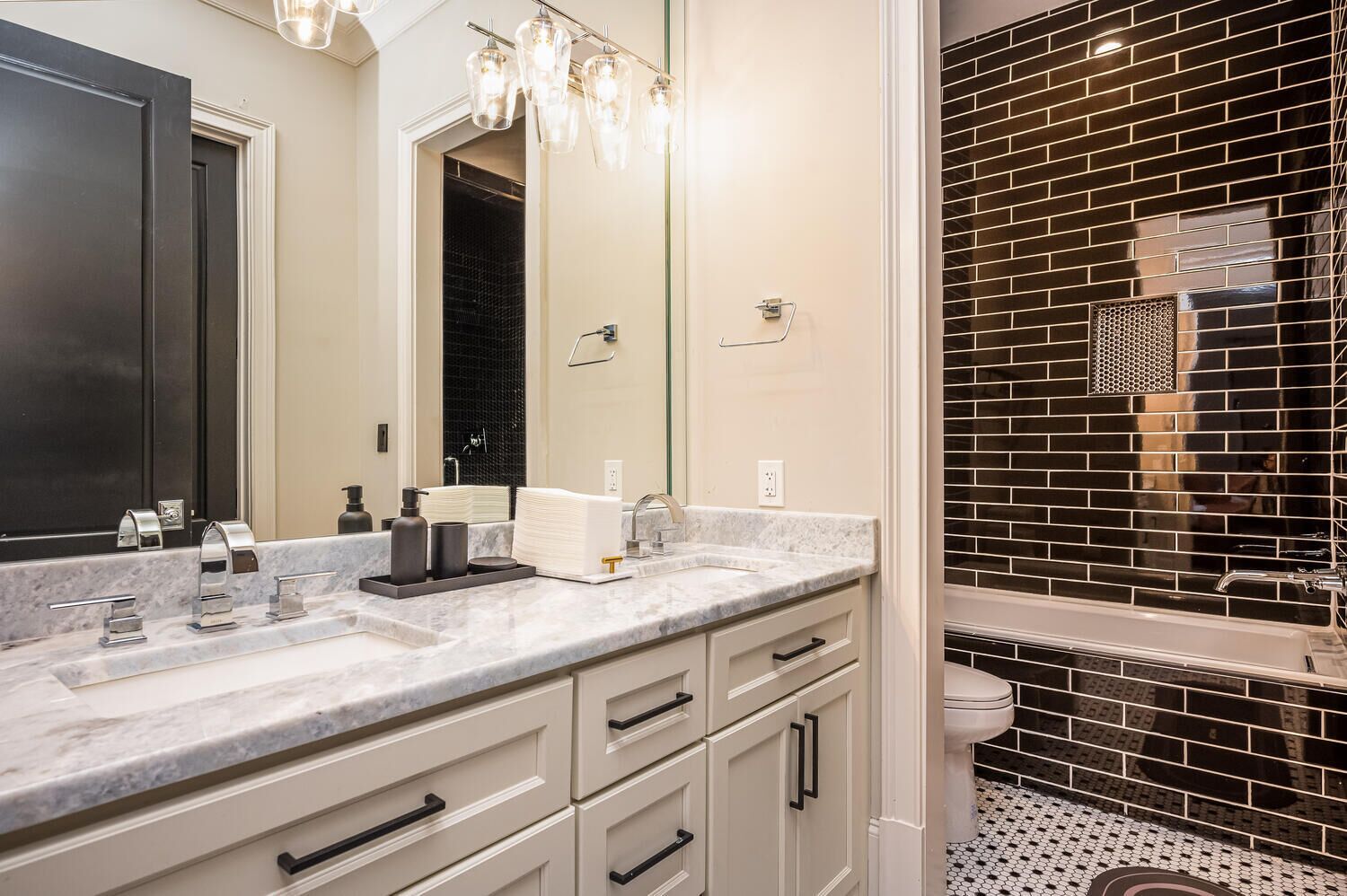 A modern bathroom with a marble vanity, a large mirror, and a black-tiled shower enclosure.