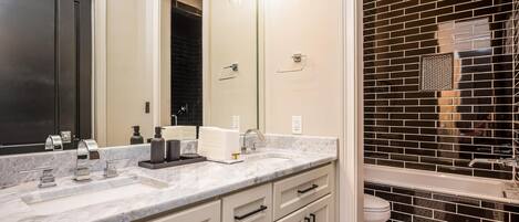 A modern bathroom with a marble vanity, a large mirror, and a black-tiled shower enclosure.