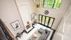 A modern living room with a fireplace, a large window with a view of greenery, and a chandelier.